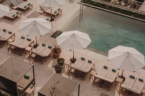 Un área de piscina en la azotea con sillones de descanso y sombrillas.