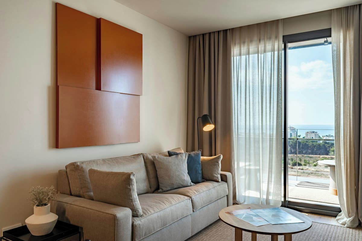 Una habitación de hotel moderna con sofá, una mesa y vistas de la ciudad a través de amplias ventanas.