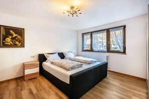 A bedroom with a bed, a nightstand, a painting, a window with curtains, and a radiator.