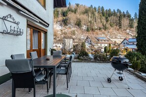 Eine Terrasse mit Tisch und Stühlen, einem Grill und Blick auf Häuser und Bäume im Hintergrund.