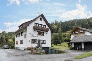 A white building with a balcony, a sign reading 'Raiffeisen Haus Wichstrand,' and a parking area.