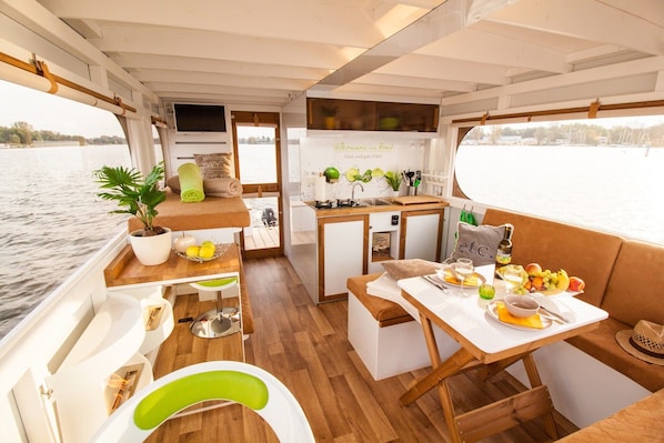 A compact boat interior with a dining area, kitchenette, and a potted plant.