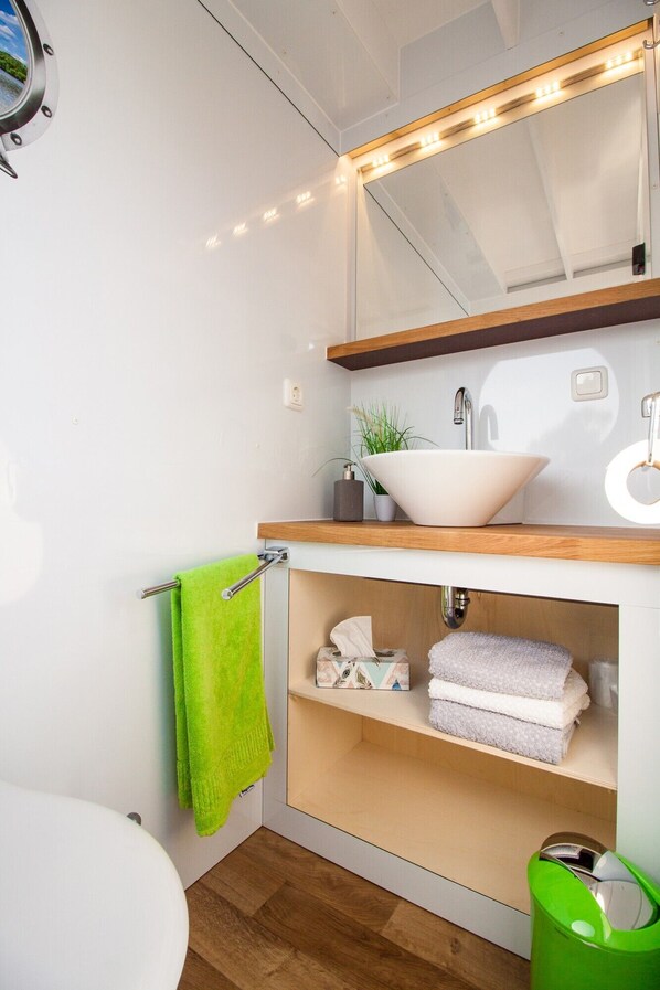 Een badkamer met een witte wasbak, een spiegel erboven, een groene handdoek en een groene prullenbak.