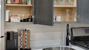 A modern kitchen with grey cabinets, a stainless steel sink, and a coffee maker. - Barnwood Suite · Romantic getaway on Main Street - Barnwood Suite (Berlin)