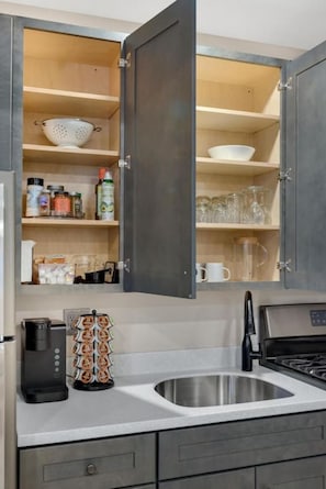 A modern kitchen with grey cabinets, a stainless steel sink, and a coffee maker.