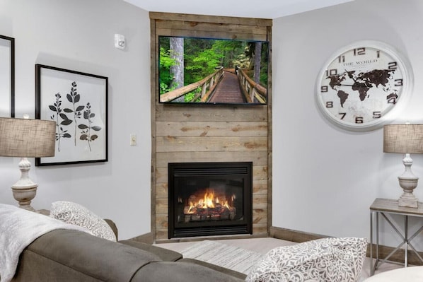 A living room with a fireplace, a television mounted above it, and a world clock on the wall.