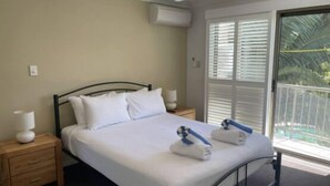 A bedroom with a bed, two bedside tables, a ceiling fan, and a window with blinds. - Quiet Noosaville Garden Retreat, Pool, Walk to River & Dining (Noosaville)
