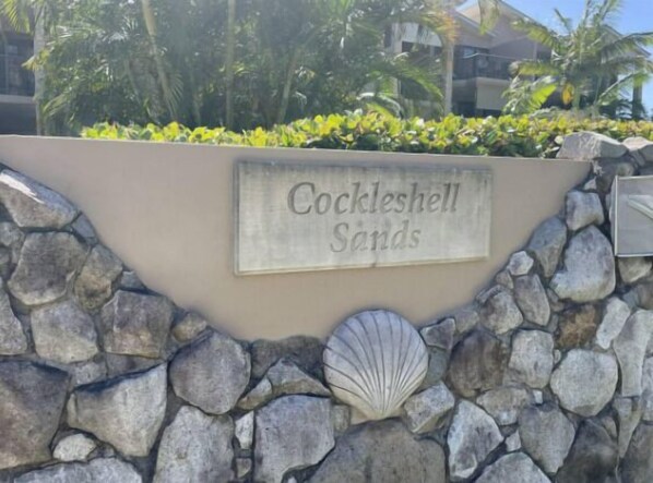 En skylt med texten ”Cockleshell Sands”, en stenmur och en dekoration i form av ett snäckskal.