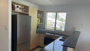 A modern kitchen with a stainless steel refrigerator, wooden cabinets, a black countertop, and a window providing natural light. - Quiet Noosaville Garden Retreat, Pool, Walk to River & Dining (Noosaville)