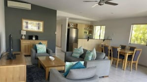 A modern living room with a grey sofa set, a wooden coffee table, and a dining area with a wooden table and chairs. - Quiet Noosaville Garden Retreat, Pool, Walk to River & Dining (Noosaville)