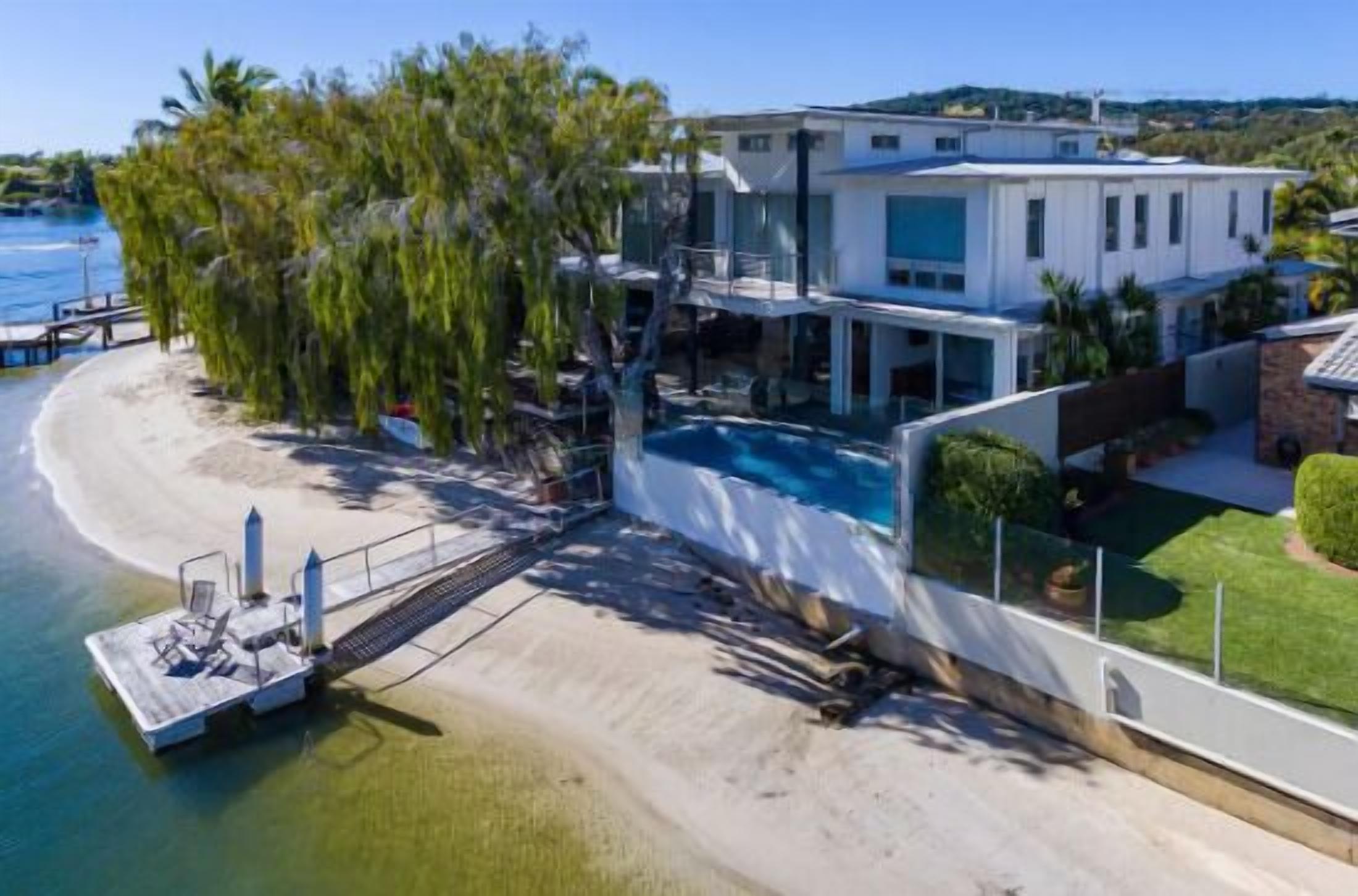 A modern beachfront property with a swimming pool, a dock, and a well-maintained lawn.