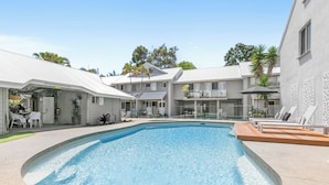 A swimming pool with a curved edge, surrounded by a patio area with outdoor furniture. - Experience the laid-back Noosa lifestyle! (Noosa)