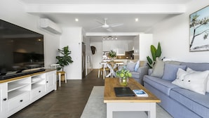 A modern living room with a sofa, coffee table, TV, and kitchen in the background. - Experience the laid-back Noosa lifestyle! (Noosa)