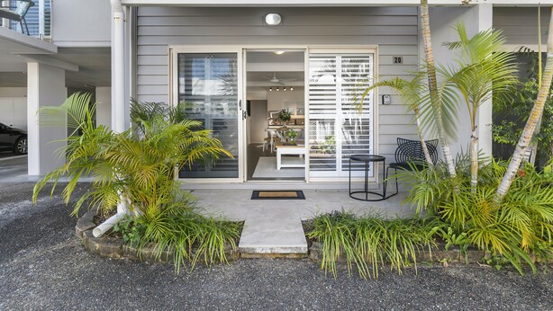 A modern two-story house with a covered porch, a sliding glass door entrance, and a small outdoor seating area with a table and chairs. - Experience the laid-back Noosa lifestyle! (Noosa)