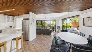 Una cocina moderna con una isla central, un comedor con una mesa grande y sillas, y vistas al exterior a través de amplios ventanales.