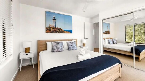 Un dormitorio moderno con una cama grande, una mesita de noche, un ventilador de techo y un cuadro de un faro.