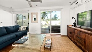 Una sala de estar moderna con un sofá azul oscuro, una mesa de centro de cristal, un mueble de madera y un televisor de pantalla plana grande.