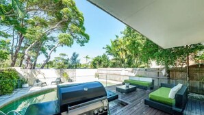 Terraza exterior con una parrilla, zona de estar y una piscina.