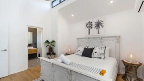 Une chambre à coucher avec un grand lit, une table de chevet, une plante en pot et une œuvre d’art accrochée au mur.