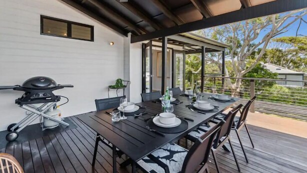 Un espace extérieur abrité, aménagé pour les repas, avec un barbecue, une table pour quatre personnes et une vue sur les arbres environnants.