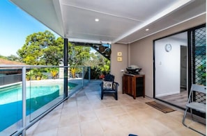Un balcon doté d’une balustrade en verre, offrant une vue sur une piscine et une végétation luxuriante.
