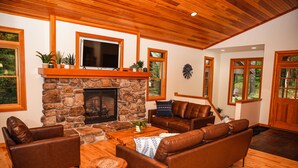 Ein gemütliches Wohnzimmer mit Kamin aus Stein, Ledersofas und Holzboden.