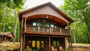 Eine zweistöckige Holzhütte mit Balkon, umgeben von einem Wald.