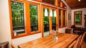 Ein Holzespeisesaal mit Stühlen, einer Blumenvase und großen Fenstern mit Blick auf Bäume.