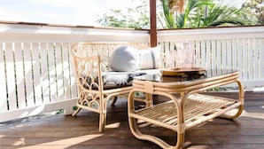 Una silla de mimbre con cojines y una mesa de vidrio en una terraza de madera.