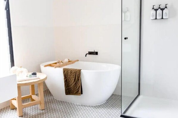 Un baño moderno con una bañera independiente, un taburete de madera y un box de ducha de vidrio.