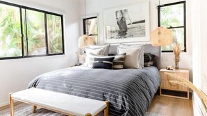 Un dormitorio con cama, una banca, mesita de noche y ventana con vistas a zonas verdes.
