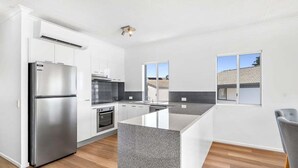A modern kitchen with white cabinets, a stainless steel refrigerator, a built-in oven, and a large island with a granite countertop.