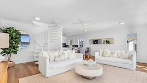A spacious living area with a white staircase, two white sofas, a round coffee table, and a view of the sea.
