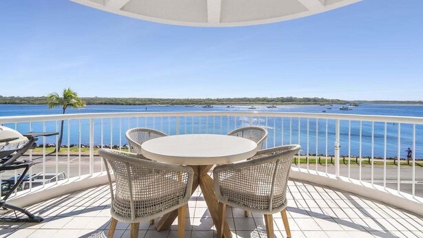 A balcony with a table and chairs, overlooking a body of water with boats.