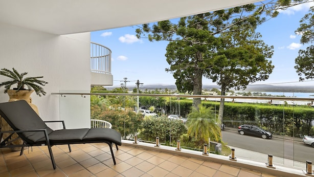 A balcony with a black lounge chair, a potted plant, and a view of a road and trees. - Light, bright and airy with breathtaking views of Noosa Heads! (Noosa)