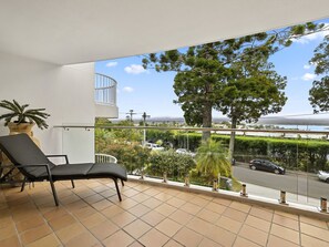 A balcony with a black lounge chair, a potted plant, and a view of a road and trees. - Light, bright and airy with breathtaking views of Noosa Heads! (Noosa)
