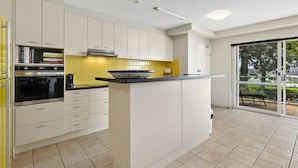 A modern kitchen with white cabinets, a built-in oven, and a large island with a bowl. - Light, bright and airy with breathtaking views of Noosa Heads! (Noosa)