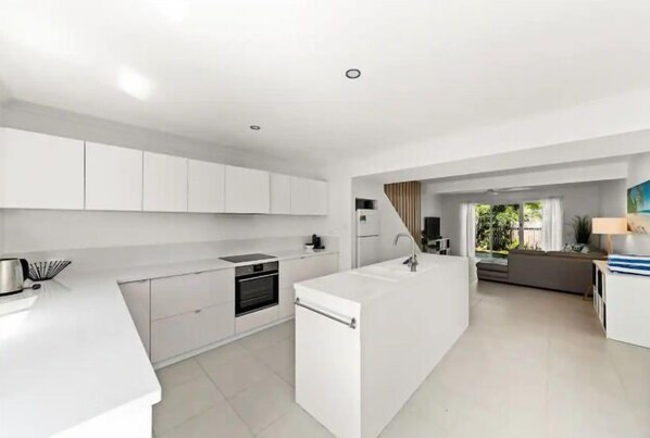 A modern kitchen with white cabinetry, a central island, and a dining area with a sofa and table.