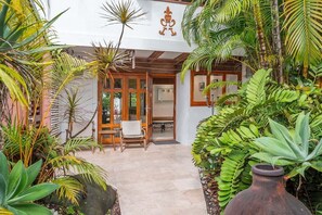 A tropical garden entrance with a wooden chair and a large vase.