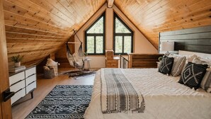 Une chambre confortable située sous les toits, avec un grand lit, un fauteuil suspendu et une vue sur l’extérieur.