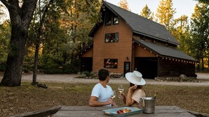Une cabane en bois avec un toit en pente, une table de pique-nique avec de la nourriture et des boissons, et un cadre naturel en pleine forêt.