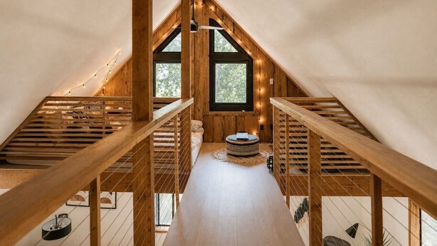 Une chambre à coucher aménagée dans un grenier, avec des poutres en bois, un plafond en pente et une fenêtre décorée de guirlandes lumineuses.