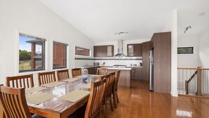 A modern kitchen with a dining area, wooden furniture, and large windows.