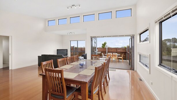A spacious dining area with a long wooden table and chairs, a television, and a view of the outdoors through large windows.