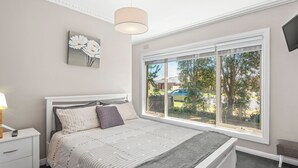 Un dormitorio con un ventanal grande, una cama con colcha a rayas, una mesita de noche con lámpara y un televisor montado en la pared.