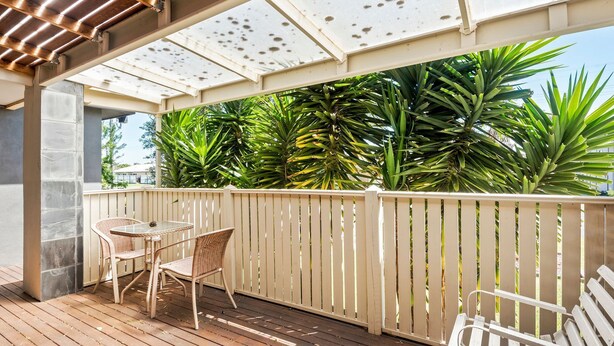 Un patio techado al aire libre con una mesa y sillas, rodeado por un cerco de madera y abundante vegetación.
