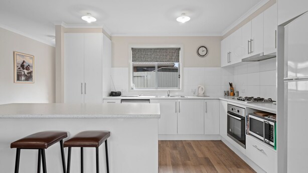 Une cuisine moderne avec des meubles blancs, un îlot central doté de tabourets, une cuisinière, un four et un four à micro-ondes.