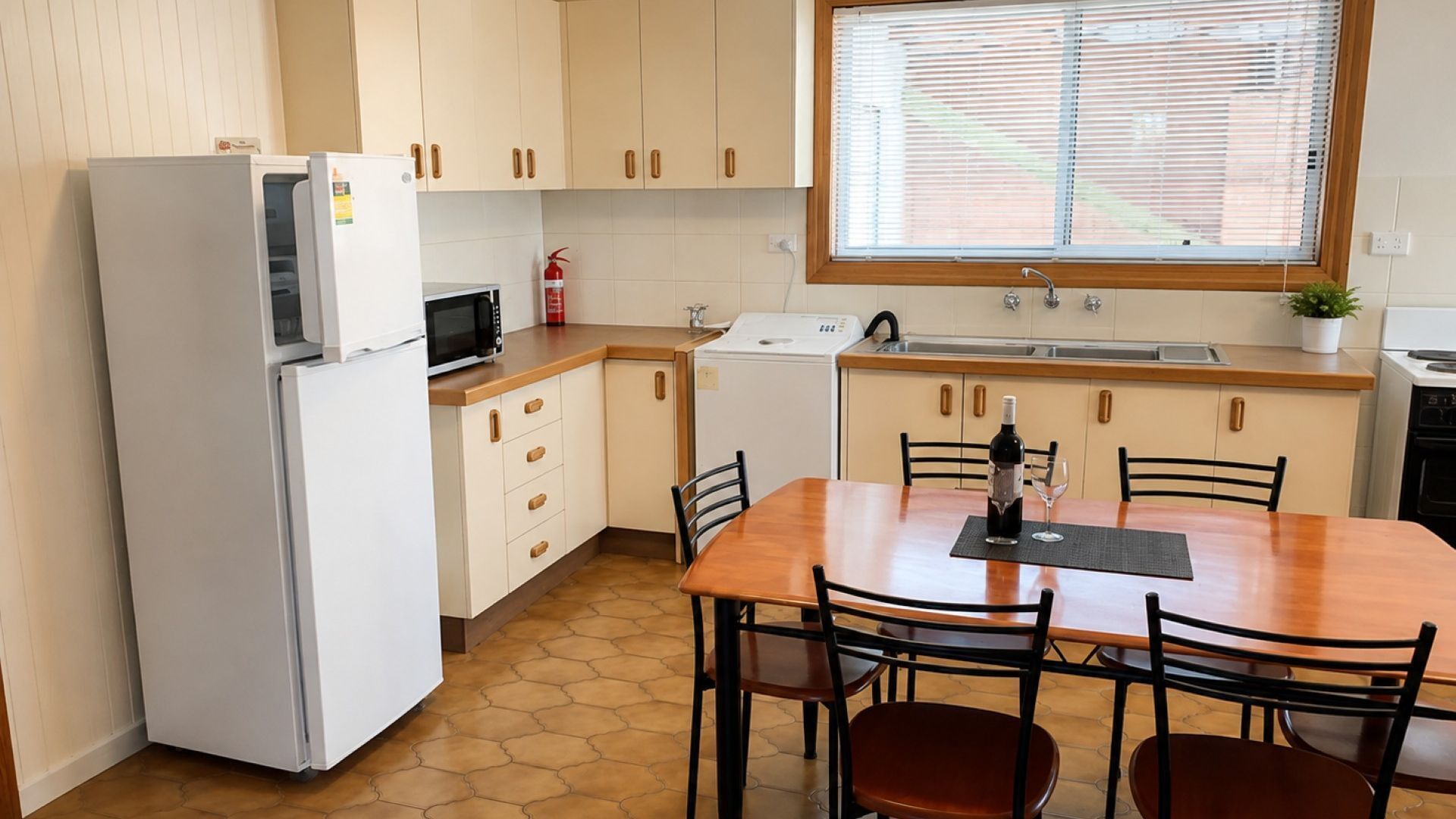 A compact kitchen with a refrigerator, microwave, and a sink. There is a dining table with chairs and a window above the sink.