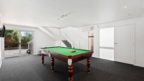 A pool table in a room with a staircase, white walls, and a door.