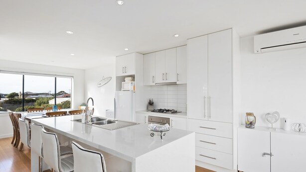 Une cuisine moderne avec des meubles blancs, un îlot central doté d’un évier et une vue sur l’extérieur.
